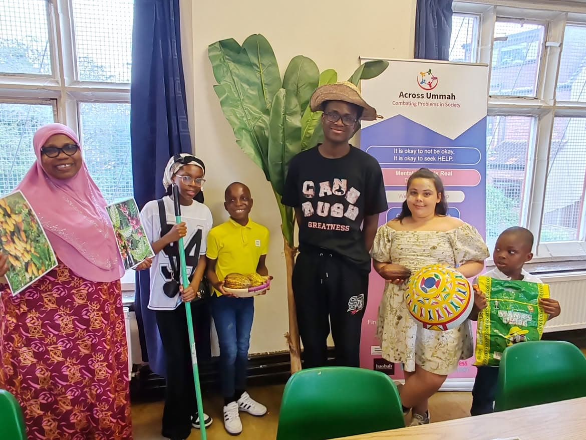 Six young people and an adult standing indoors, holding printed pictures of cocoa plants, a woven bowl and a cocoa pod.